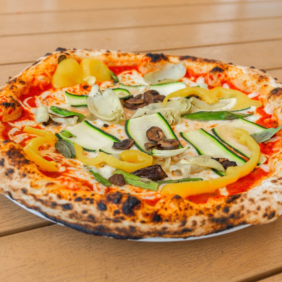 Neapolitan pizza with zucchini, yellow peppers, mushrooms, and artichoke hearts on a wooden table.