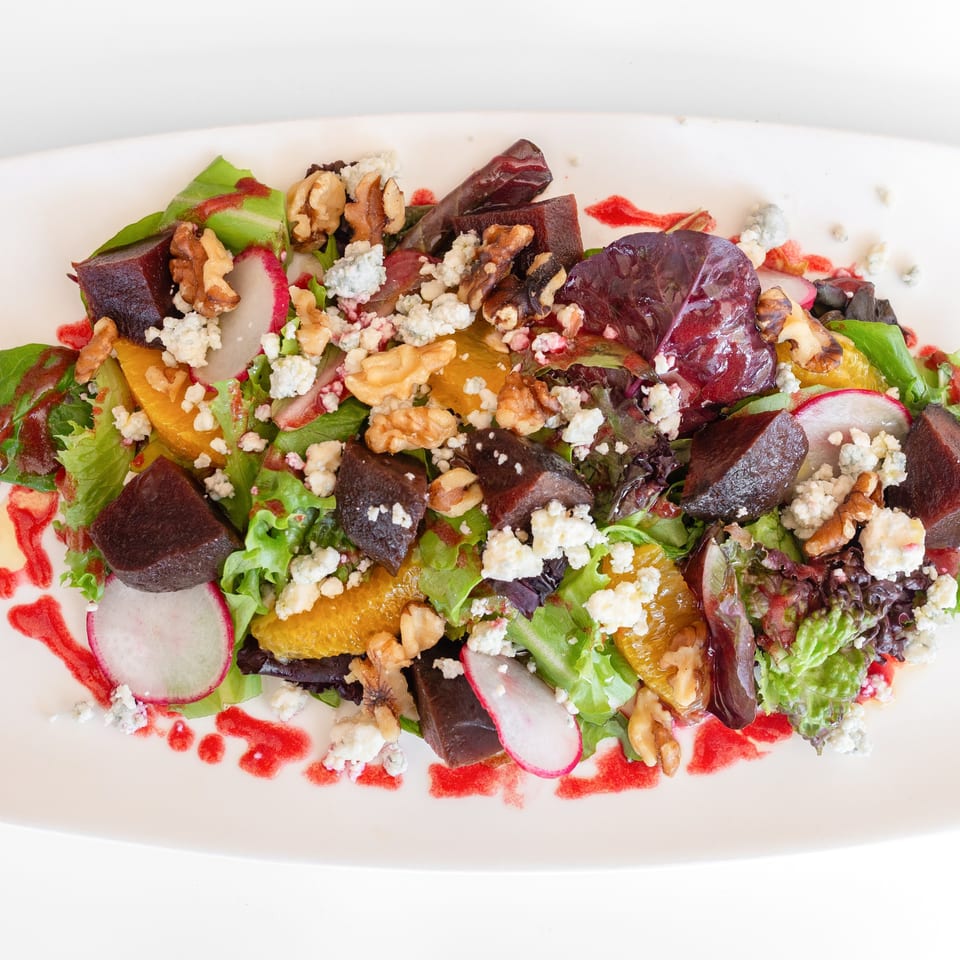 Colorful salad with beets, oranges, walnuts, blue cheese, radishes, and mixed greens on a white plate.