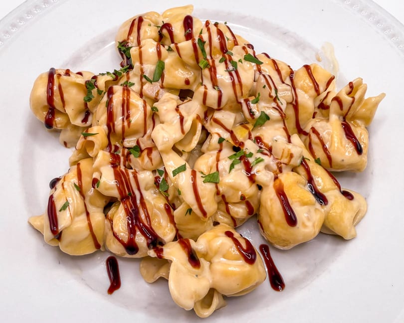 Close-up of pasta shells covered in creamy sauce, drizzled with balsamic glaze and fresh parsley.