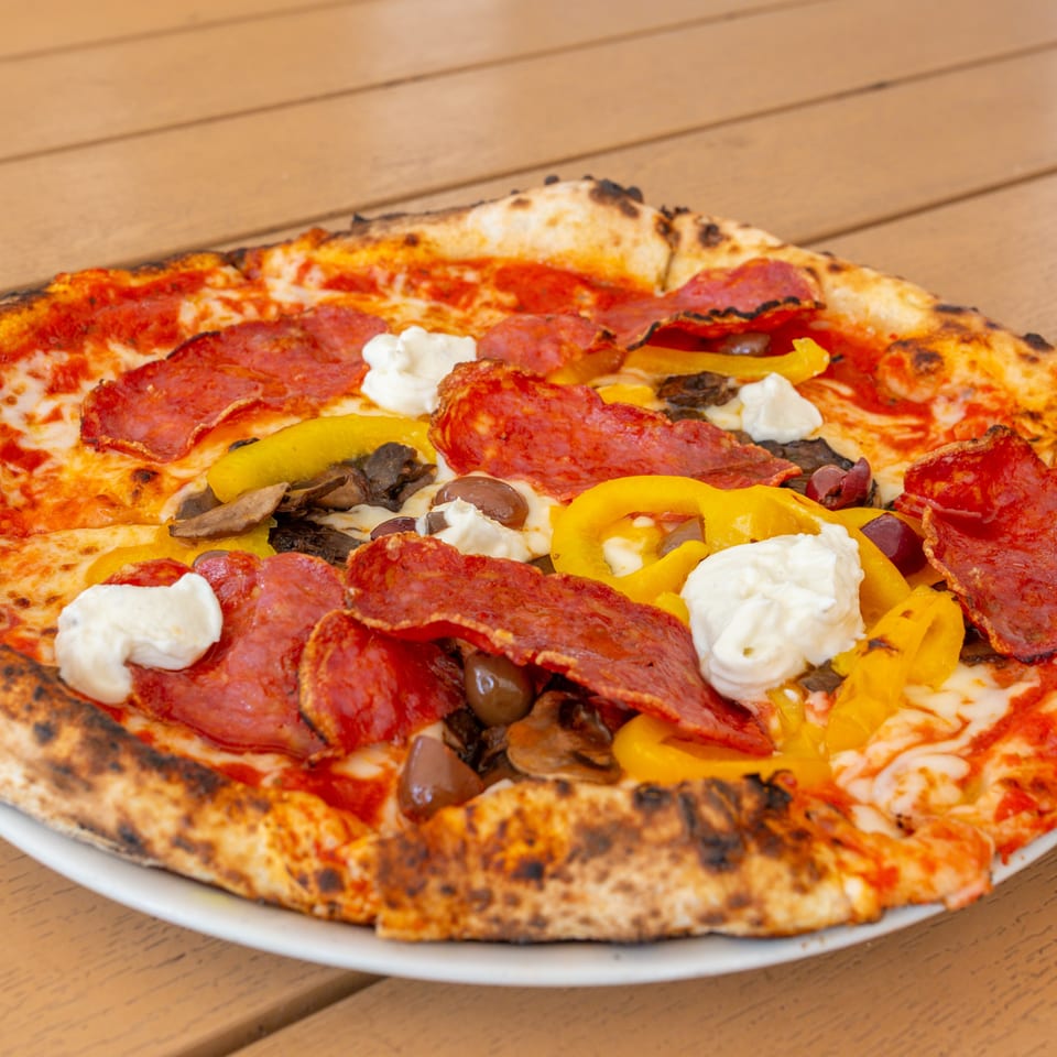 Close-up of a pizza with pepperoni, yellow peppers, mushrooms, olives, and dollops of ricotta.