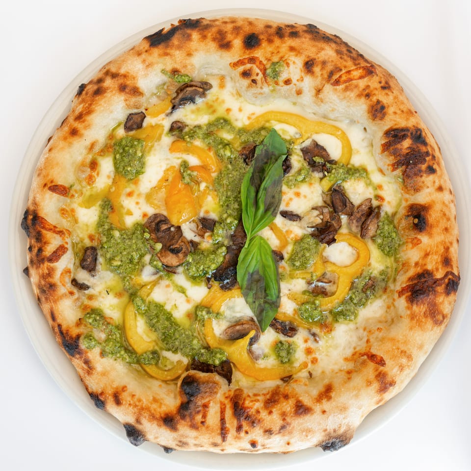 Neapolitan pizza with pesto, yellow bell peppers, mushrooms, mozzarella, and a basil garnish.