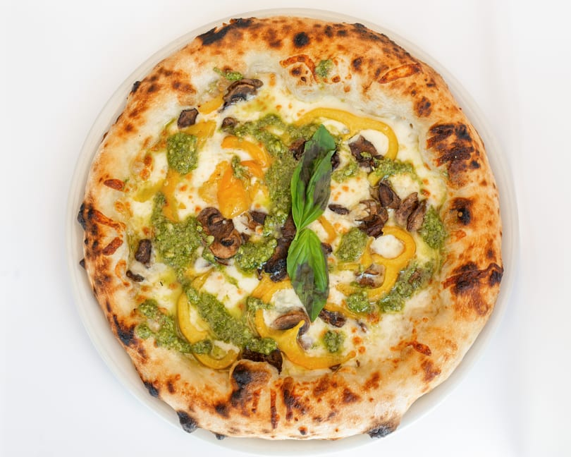 Neapolitan pizza with pesto, yellow bell peppers, mushrooms, mozzarella, and a basil garnish.