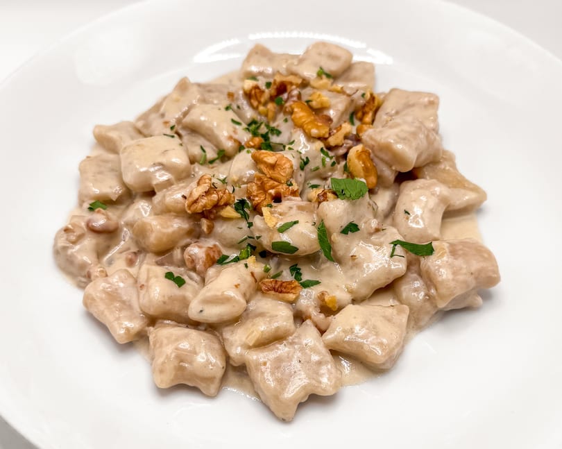 Creamy gnocchi pasta dish topped with chopped walnuts and fresh parsley on a white plate.
