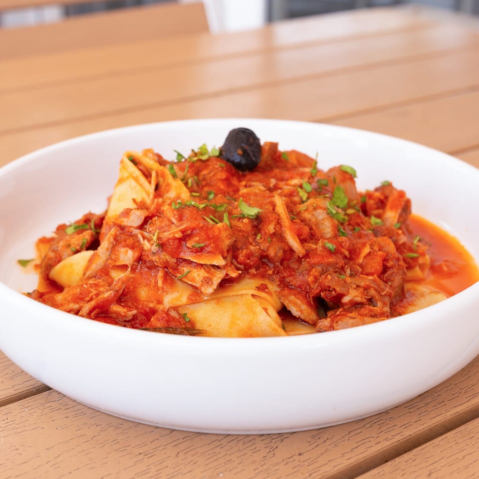 Pappardelle pasta with a rich red tomato and meat sauce, garnished with parsley and a black olive.