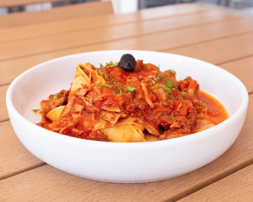 Pappardelle pasta with a rich red tomato and meat sauce, garnished with parsley and a black olive.