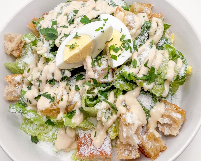 Caesar salad with romaine lettuce, croutons, parmesan, creamy dressing, parsley, and hard-boiled egg.
