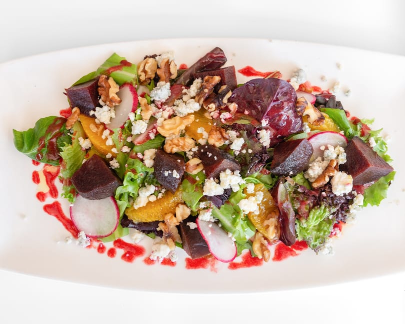 Colorful salad with mixed greens, beets, oranges, walnuts, blue cheese, and radish slices.
