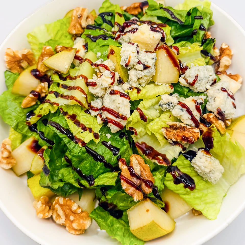 A fresh salad with green lettuce, pear slices, walnuts, blue cheese, and balsamic glaze.