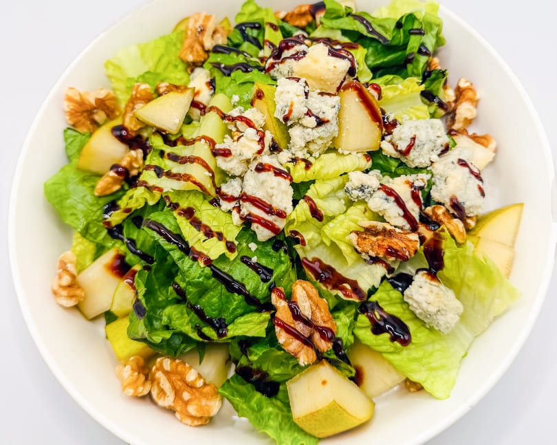 A fresh salad with green lettuce, pear slices, walnuts, blue cheese, and balsamic glaze.